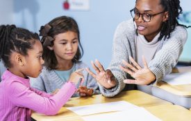A black elementary teacher with children in the classroom. They are sitting at desks having a math lesson.