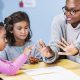 A black elementary teacher with children in the classroom. They are sitting at desks having a math lesson.