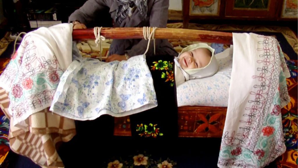 Tajik baby in gahvora and smiling at the camera.