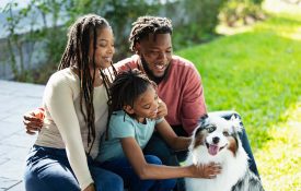 A Black family poses with their dog outside.