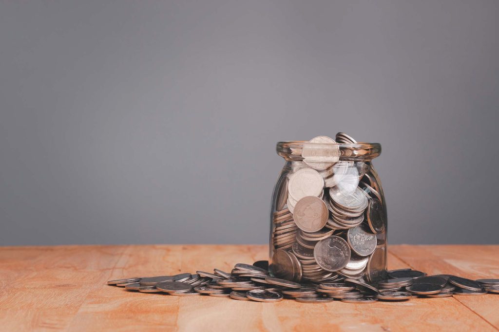 An overfilled jar of coins on a wooden table.