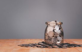 An overfilled jar of coins on a wooden table.