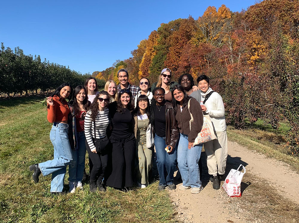 The group of lab members pose for a photo at an apple orchard, with colorful trees and a blue sky behind them.