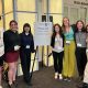 Six students and Julia Leonard pose for a photo around a sign regarding the plenary talk.