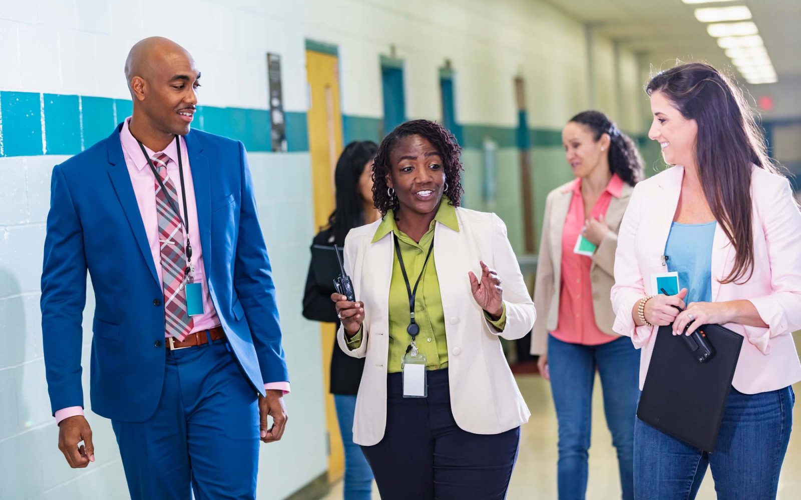 School teachers conversing as they walk through a school corridor.