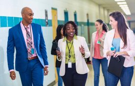 School teachers conversing as they walk through a school corridor.