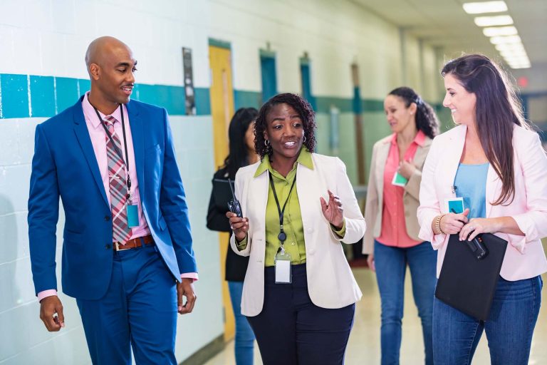 School teachers conversing as they walk through a school corridor.