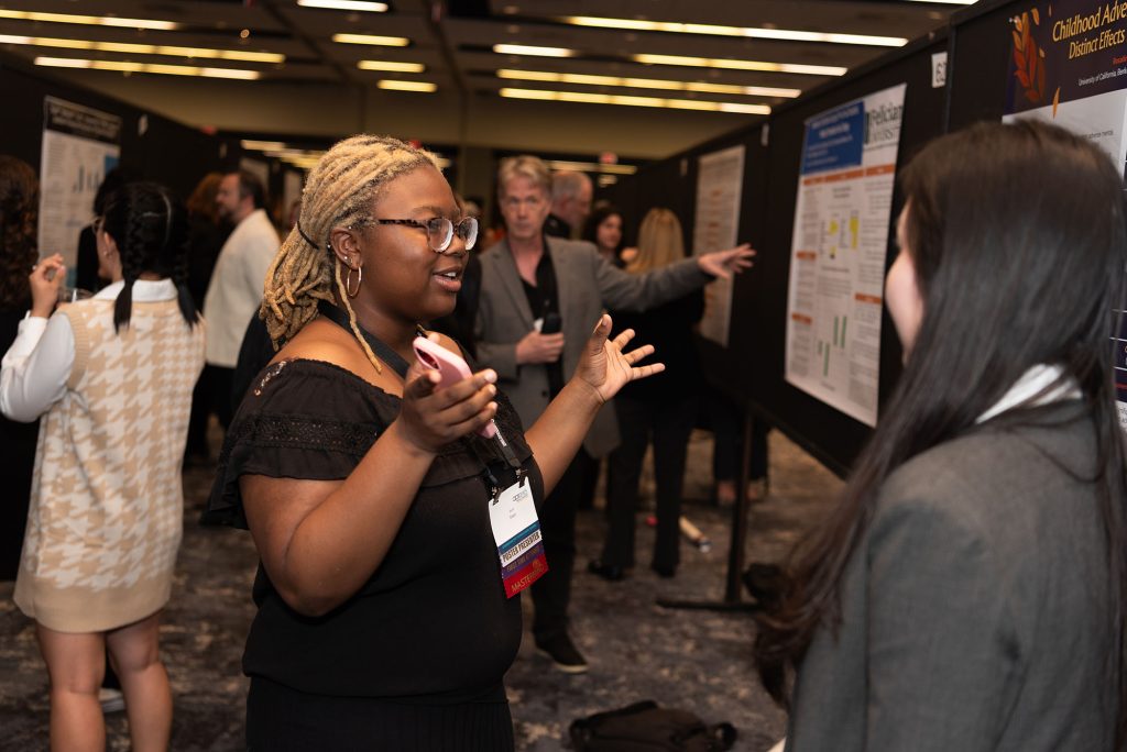 A young researcher presents in front of her poster with her hands out.