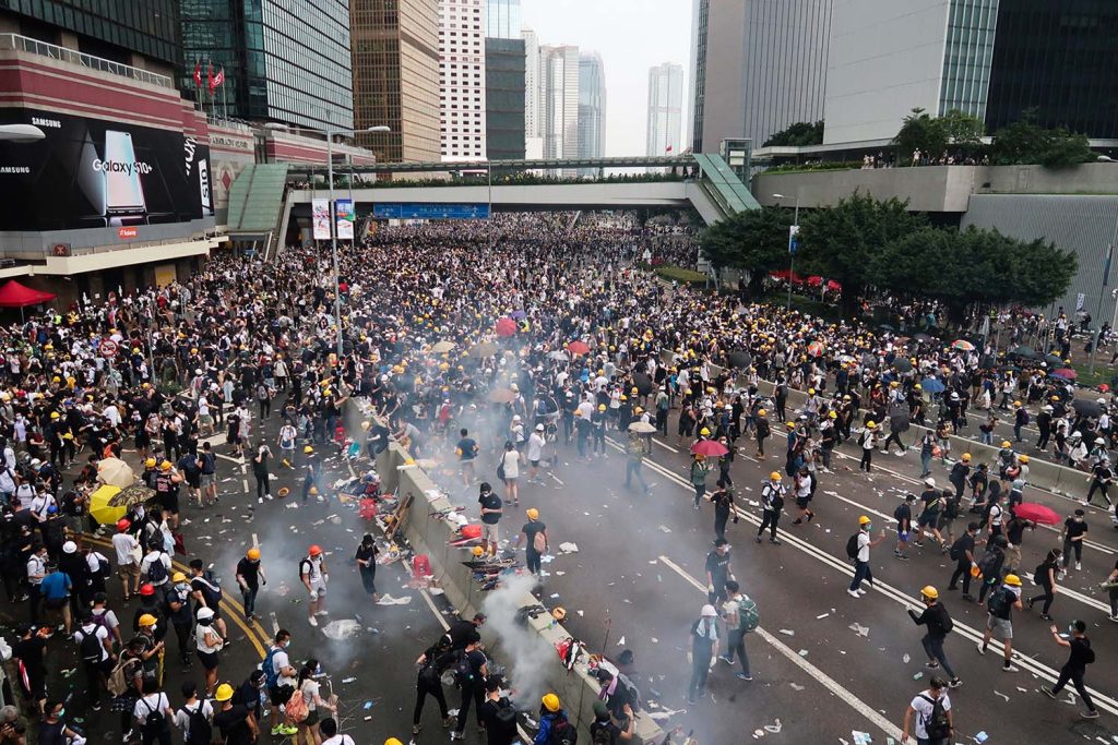 A wide shot of a large group of protestors as tear gas is deployed by police.
