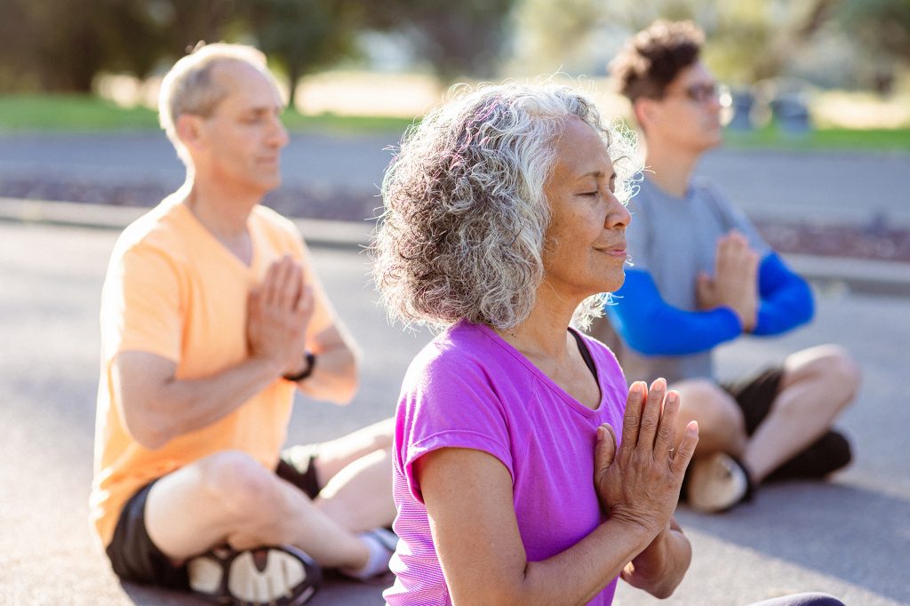 Senior woman meditating while during outdoor group fitness and yoga class