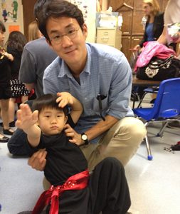 Photo of Tae-Ho Lee posing with a small child at a school.