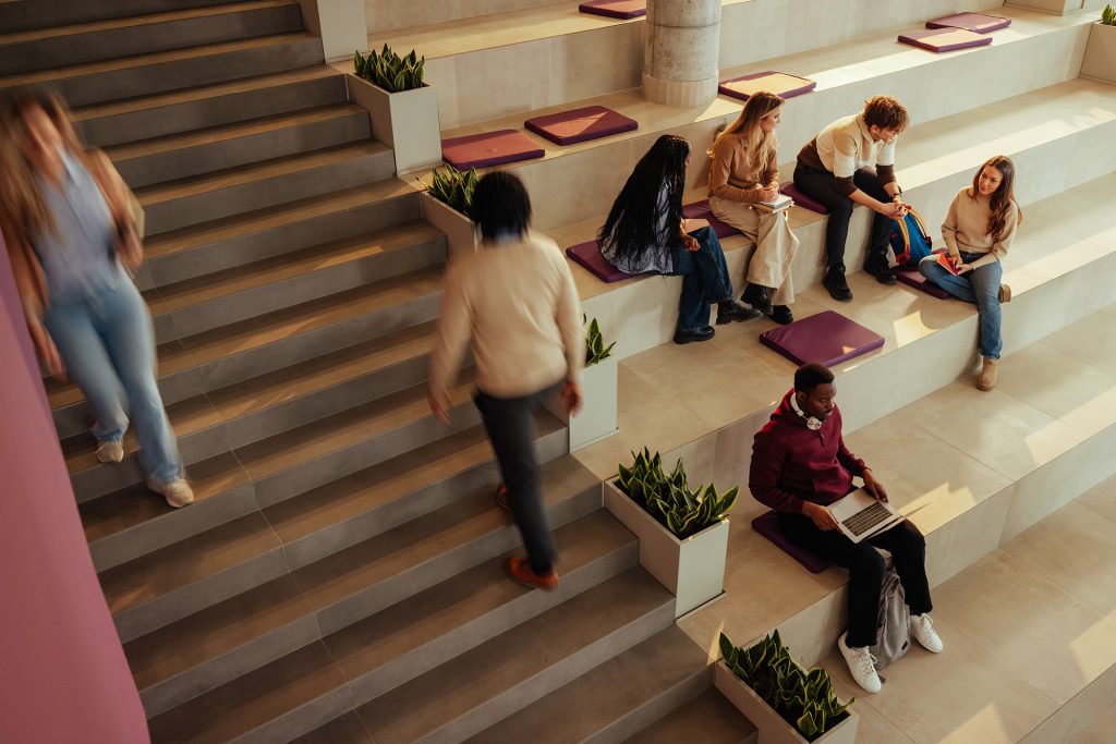 Students studying and walking on stairs in a bright, modern university hall, engaging in collaborative learning.