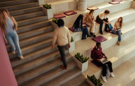 Students studying and walking on stairs in a bright, modern university hall, engaging in collaborative learning.