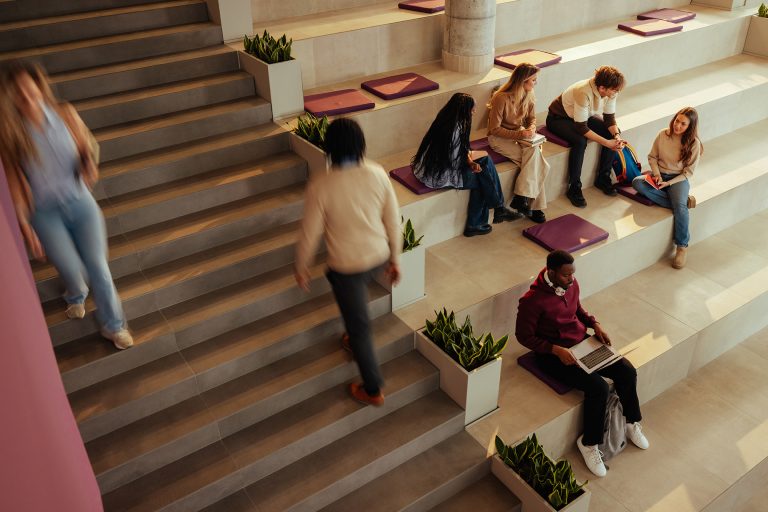 Students studying and walking on stairs in a bright, modern university hall, engaging in collaborative learning.