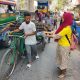 A woman hands a man a water bottle as he walks his bike by.