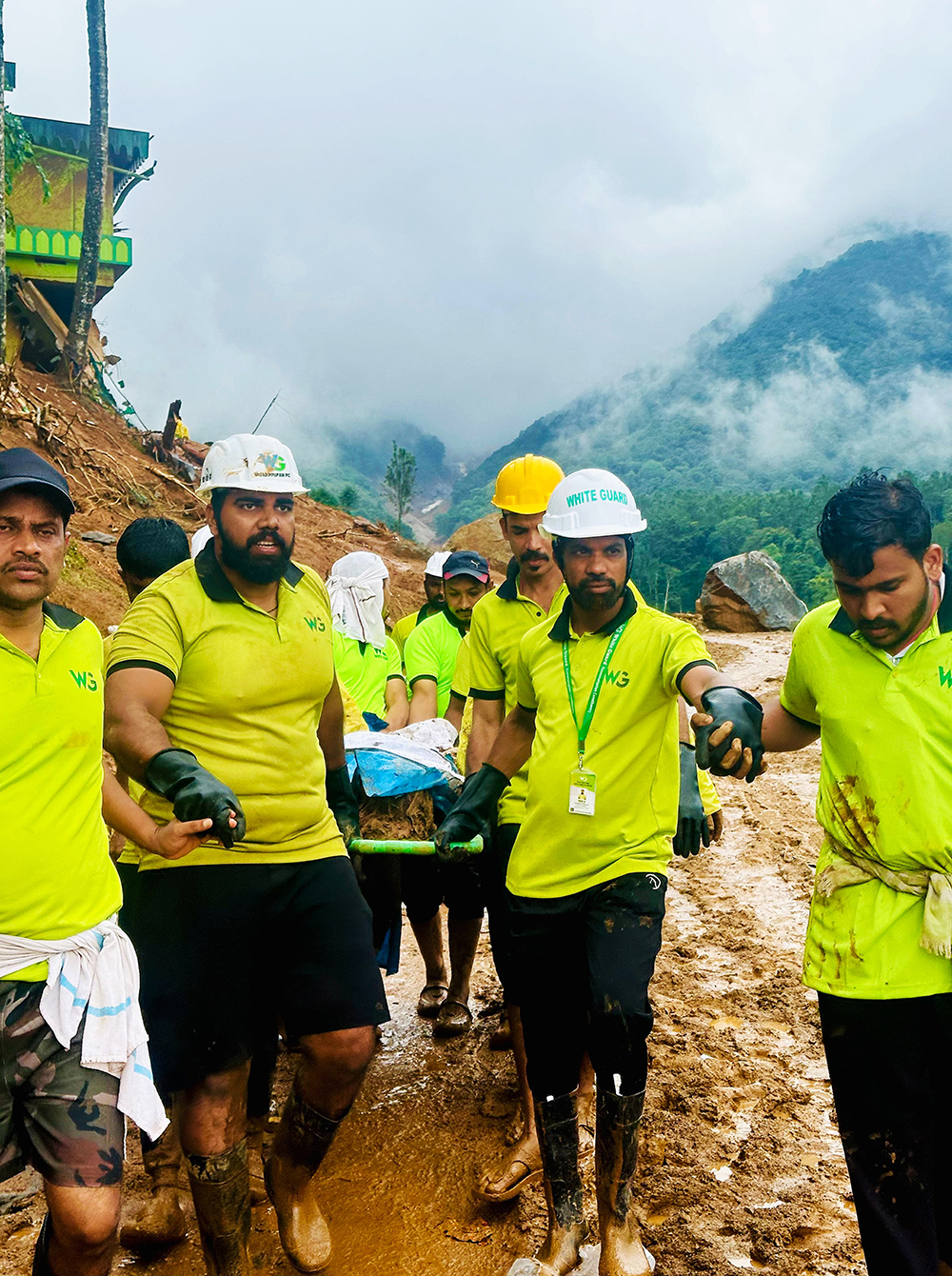 White Guard volunteers in neon shirts and construction helmets hold hands as they walk down the muddy road.