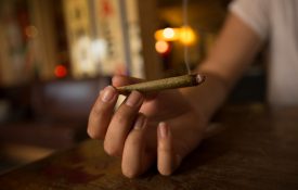Person holding a cannabis joint that is lit.