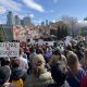 A photograph of a crowd of people at the Stand Up For Science protest in Seattle, Washington on 07 March 2025. Many people are holding signs, one of which says "Science = Progress." The people in the crowd are facing a speaker on a stage. At the top left of the photograph is part of the Space Needle, an iconic landmark in Seattle.