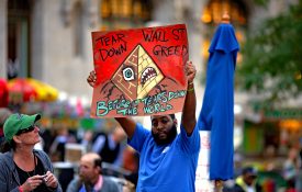 A Black man holding a protest sign during the Occupy Wall Street protest in 2011: "Tear down Wall St greed before it tears down the world."