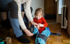 Father helping toddler get dressed in overall at hallway.