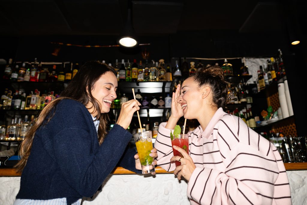 Young friends laughing enjoying drinks at bar