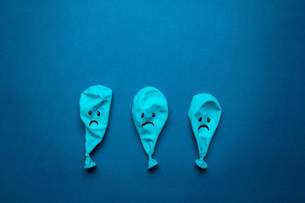Three deflated blue balloons frowning on blue background.