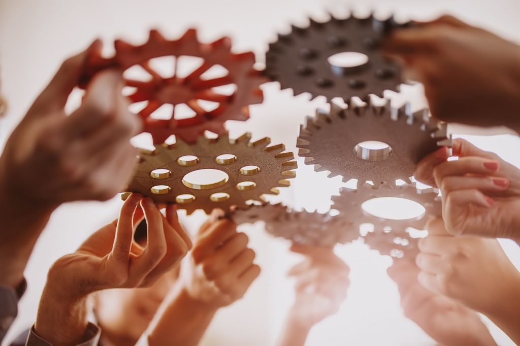 Multiple hands holding gears up toward each other.