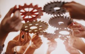 Multiple hands holding gears up toward each other.