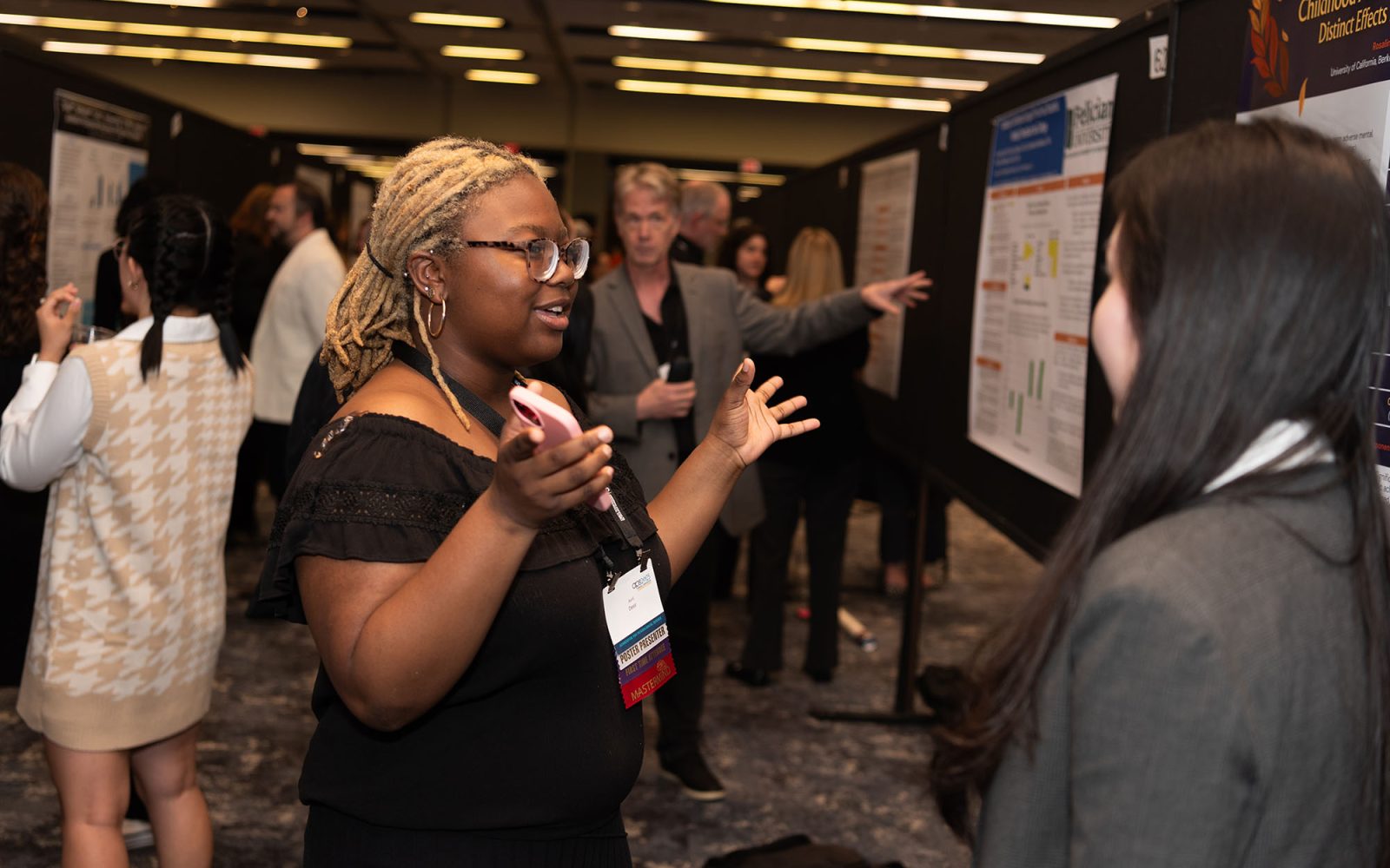 Researchers presenting their posters, talking with their hands and pointing to the poster board.