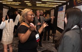 Researchers presenting their posters, talking with their hands and pointing to the poster board.