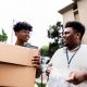 Two young volunteers work together during a community donation event, carrying cardboard boxes and communicating with enthusiasm.