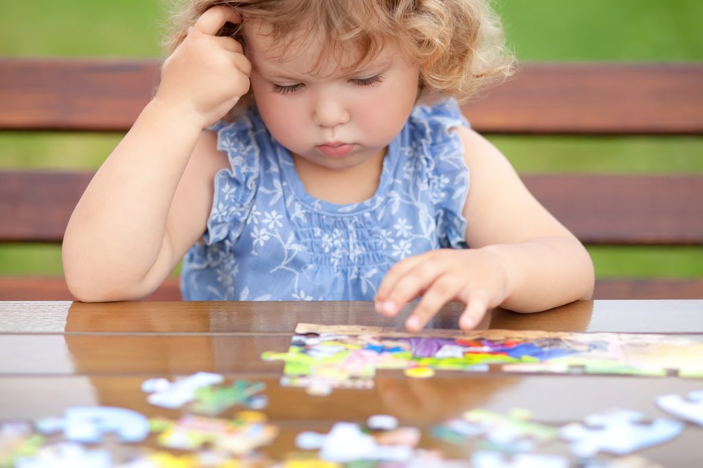 Toddler girl, solving puzzle on a table.