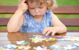 Toddler girl, solving puzzle on a table.