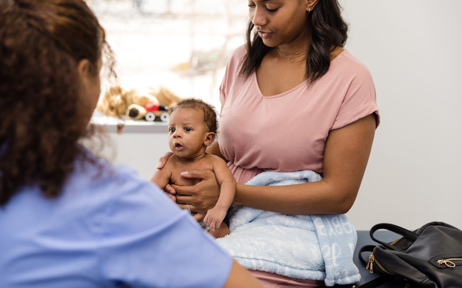 Newborn boy sits in his mother's lap and attentively listens to a healthcare professional while she talks.