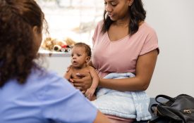 Newborn boy sits in his mother's lap and attentively listens to a healthcare professional while she talks.