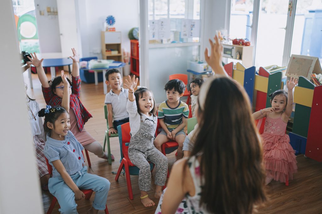 Preschool student raised hands in the class answering questions.