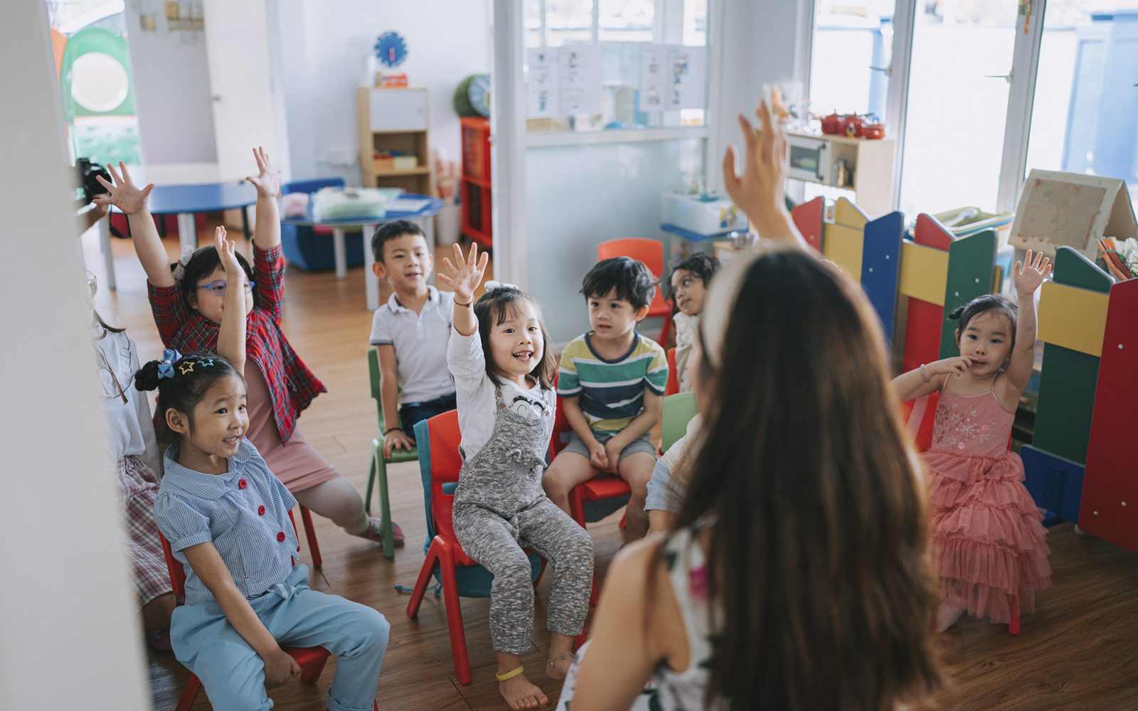 Preschool student raised hands in the class answering questions.