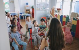 Preschool student raised hands in the class answering questions.