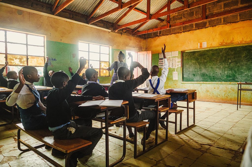 Female Teacher teaching a class of high school students in uniform in a rural school in Africa Malealea, Lesotho. Rear view of the learners with their hands raised.