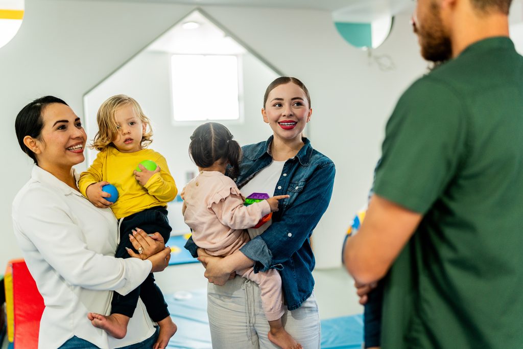 Parents carrying babies and talking at playroom.