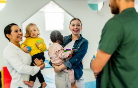 Parents carrying babies and talking at playroom.